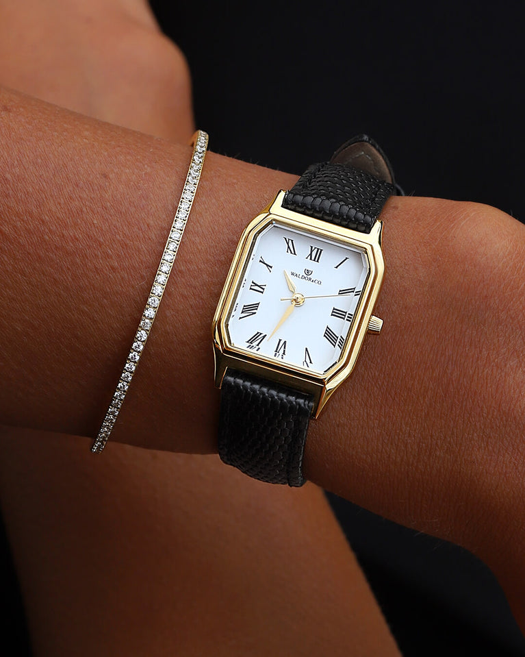 A square womens watch in 22k gold from Waldor & Co. with white Diamond Cut Sapphire Crystal glass dial. Strap in black Genuine leather. Seiko movement. The model is Eternal 22 Varenna. 