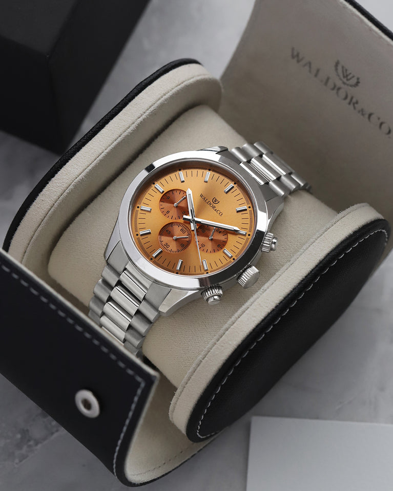 A round mens watch in rhodium-plated silver from Waldor & Co. with orange sunray dial and a second hand. Seiko movement. The model is Chrono 44 Como 44mm.