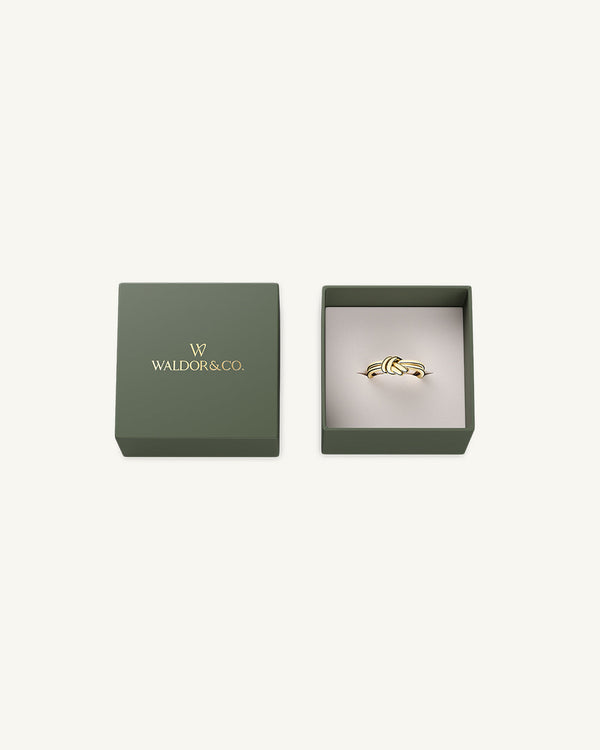 A polished stainless steel ring in 14k gold from Waldor & Co. One size. The model is Dual Knot Ring.