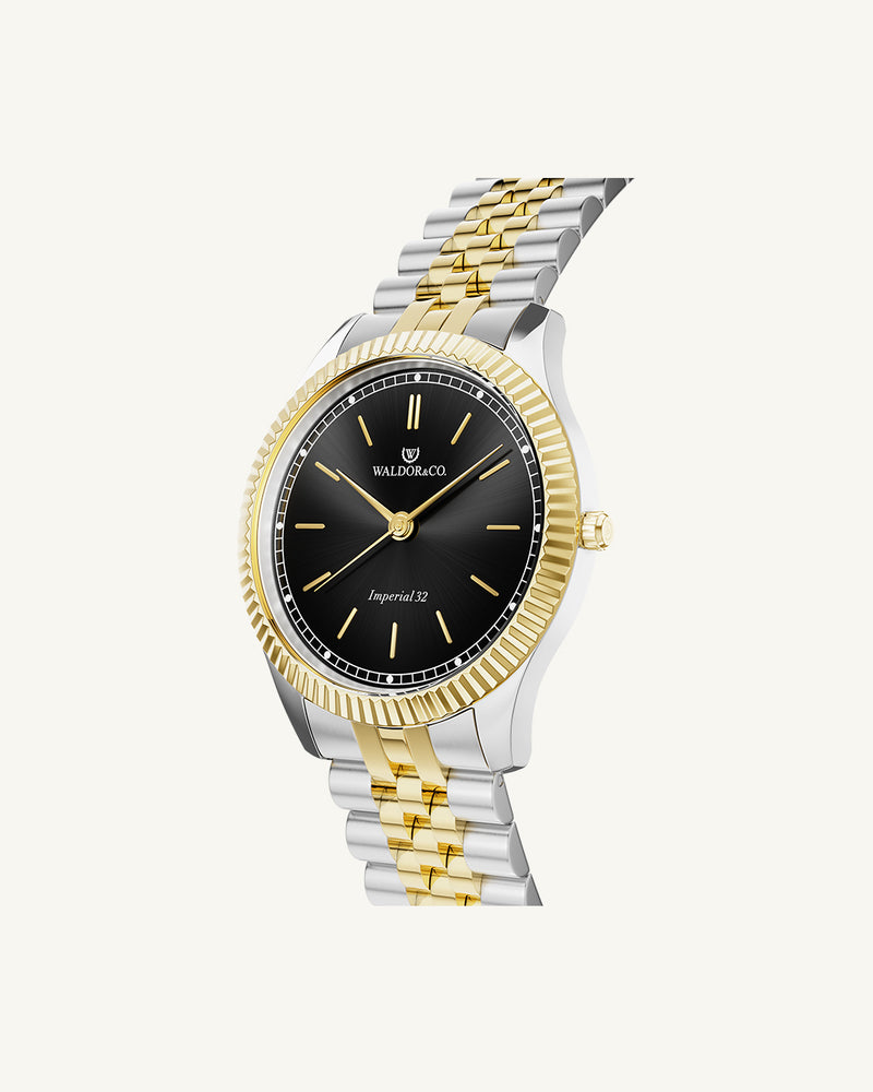 A round womens watch in silver and 14k gold from Waldor & Co. with black sunray dial and a second hand. Seiko movement. The model is Imperial 32 Positano 32mm.