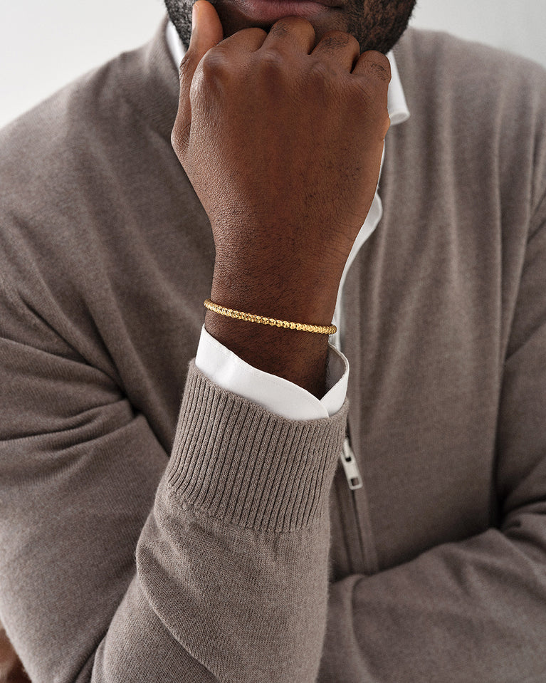 A polished stainless steel bangle in 14k gold plated from Waldor & Co. One size. The model is Noble Bangle Polished