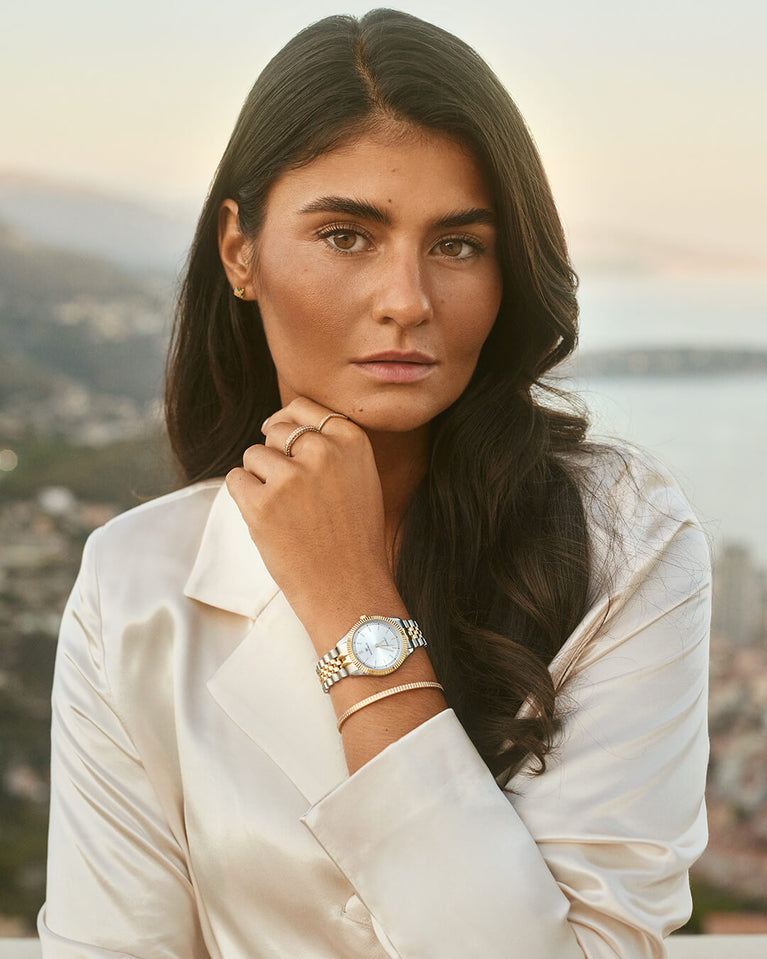 A round womens watch in silver and 22k gold from Waldor & Co. with silver sunray dial and a second hand. Seiko movement. The model is Imperial 32 Positano 32mm.