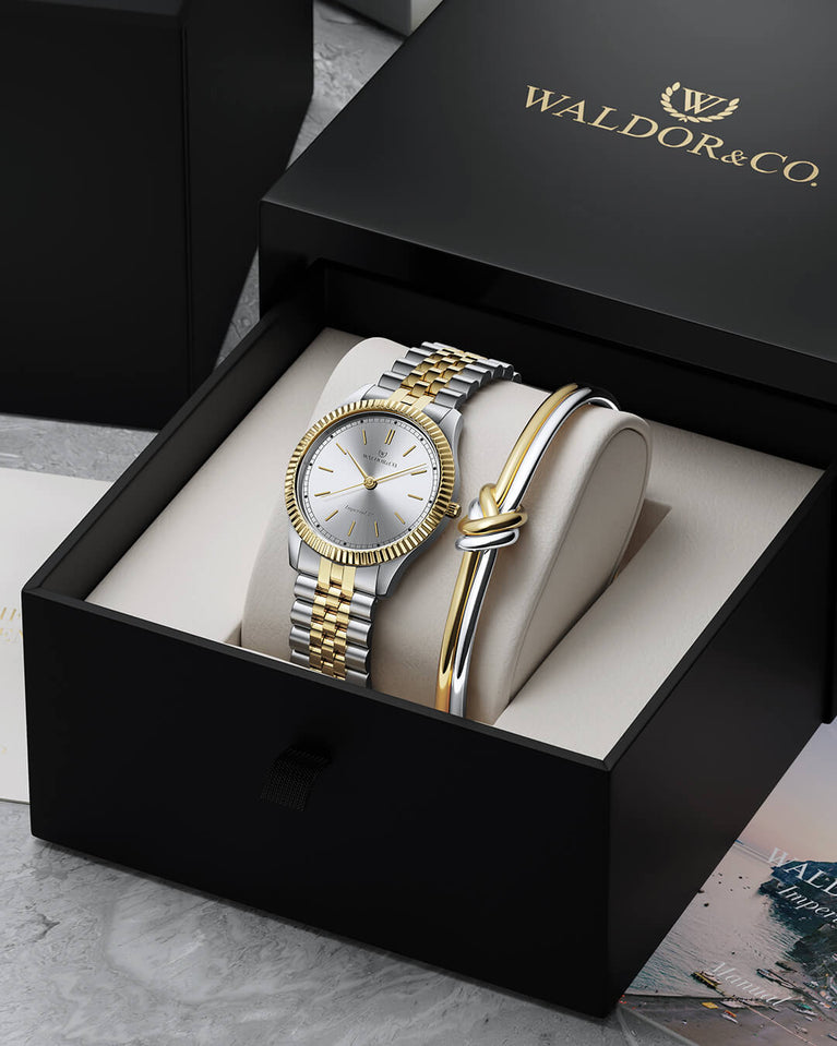 A round womens watch in silver and 22k gold from Waldor & Co. with silver sunray dial and a second hand. Seiko movement. The model is Imperial 32 Positano 32mm.